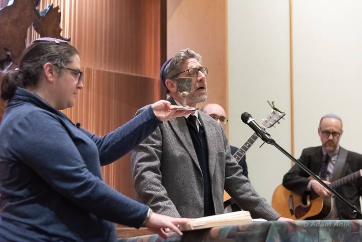 Rabbi Ariann Weitzman holds the cup of wine for Rabbi David Greenstein's prayers at the vigil at B'nai Keshet  to mourn the victims of the Tree of Life massacre Sat. night, Oct. 27.